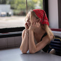  A young woman with blonde hair wearing a red bandana sits at a diner booth.